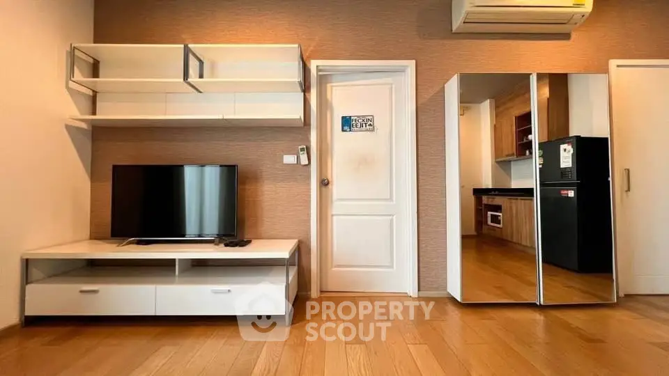 Modern living room with sleek TV unit and mirrored wardrobe, adjacent to a stylish kitchen with built-in appliances.