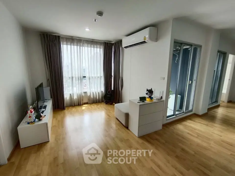 Spacious modern living room with wooden flooring and large window, featuring air conditioning and stylish decor.