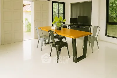 Modern dining area with sleek table and chairs, featuring large windows and lush greenery view.