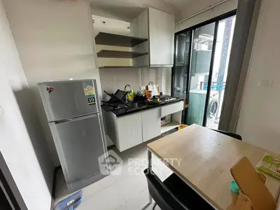 Modern kitchen with sleek cabinets, dining table, and balcony access, featuring a fridge and washing machine.