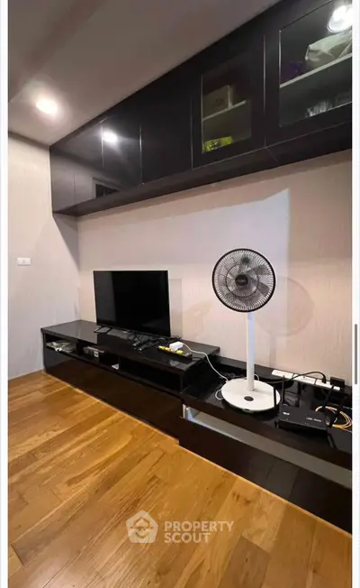 Modern living room with sleek black cabinetry and wooden flooring, featuring a TV and fan for comfort.