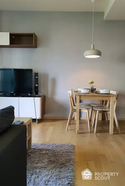 Cozy and inviting living space with modern furnishings, warm wooden flooring, and a simplistic dining set illuminated by a stylish pendant light.