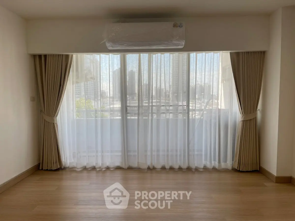 Spacious living room with large window and city view, featuring elegant curtains and wooden flooring.