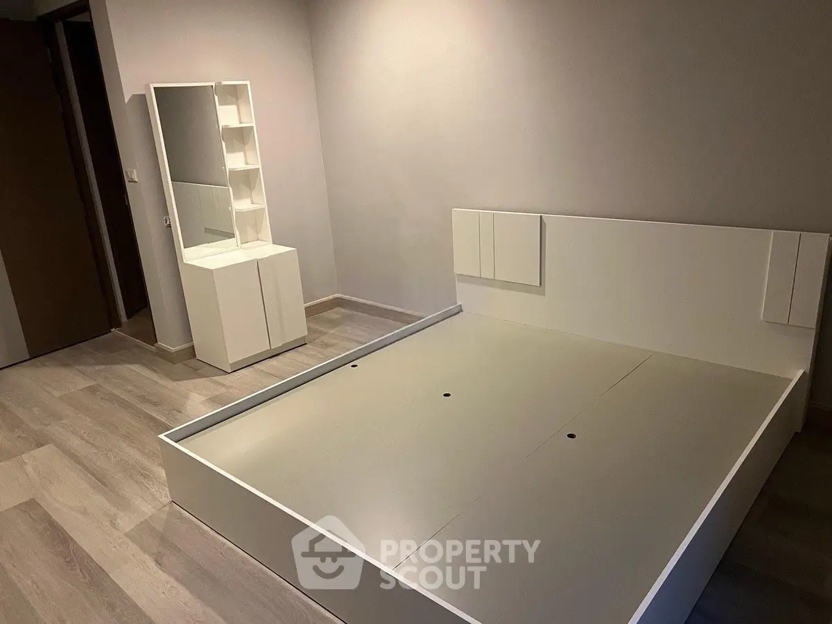 Modern minimalist bedroom with sleek white furniture and wooden flooring.