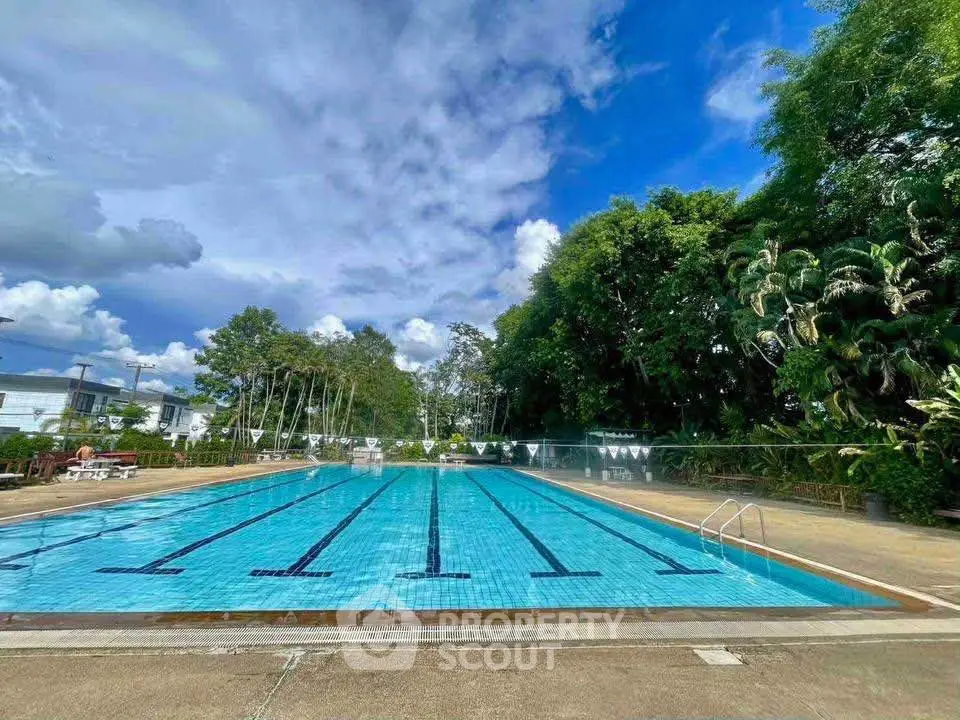 Stunning outdoor pool with lush greenery and clear blue skies, perfect for relaxation and leisure.
