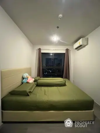 Cozy bedroom with green bedding and city view, featuring air conditioning and plush toys.