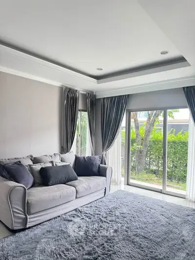 Elegant living room with large windows and plush gray sofa, offering a serene garden view.