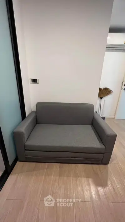 Modern compact gray sofa in a stylish minimalist room with wooden flooring.