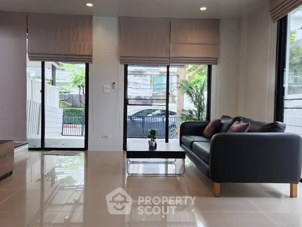 Modern living room with sleek black sofa and large windows offering natural light and garden view.