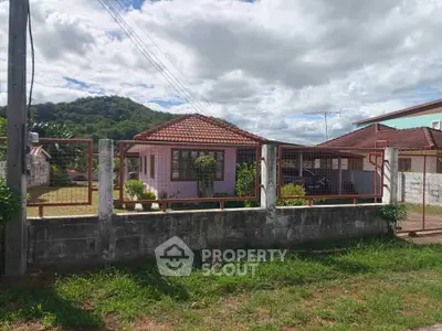 Charming single-story house with red-tiled roof and fenced yard, nestled in a scenic hillside location.