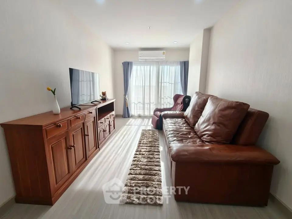 Spacious living room with leather sofa and entertainment unit, featuring natural light and modern decor.