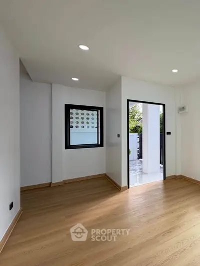 Spacious modern room with wooden flooring and large window opening to a garden view.