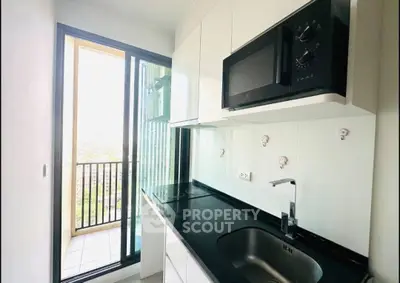 Modern kitchen with sleek design and balcony view, featuring microwave and electric stove.