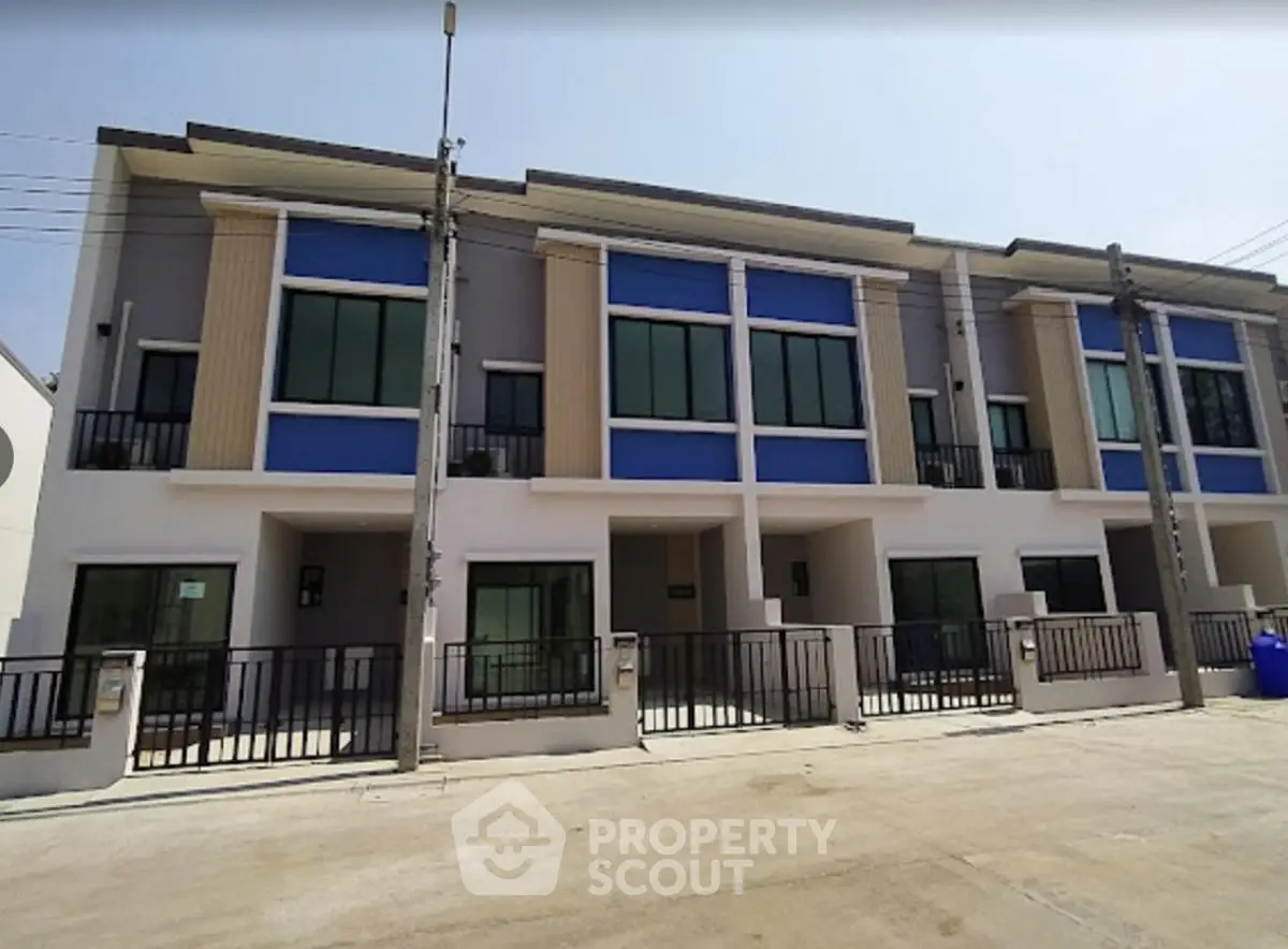 Modern townhouse exterior with large windows and balconies in a sunny neighborhood.