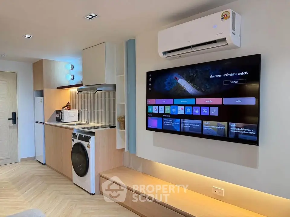 Modern living room with sleek kitchen, washing machine, and wall-mounted TV in stylish apartment.