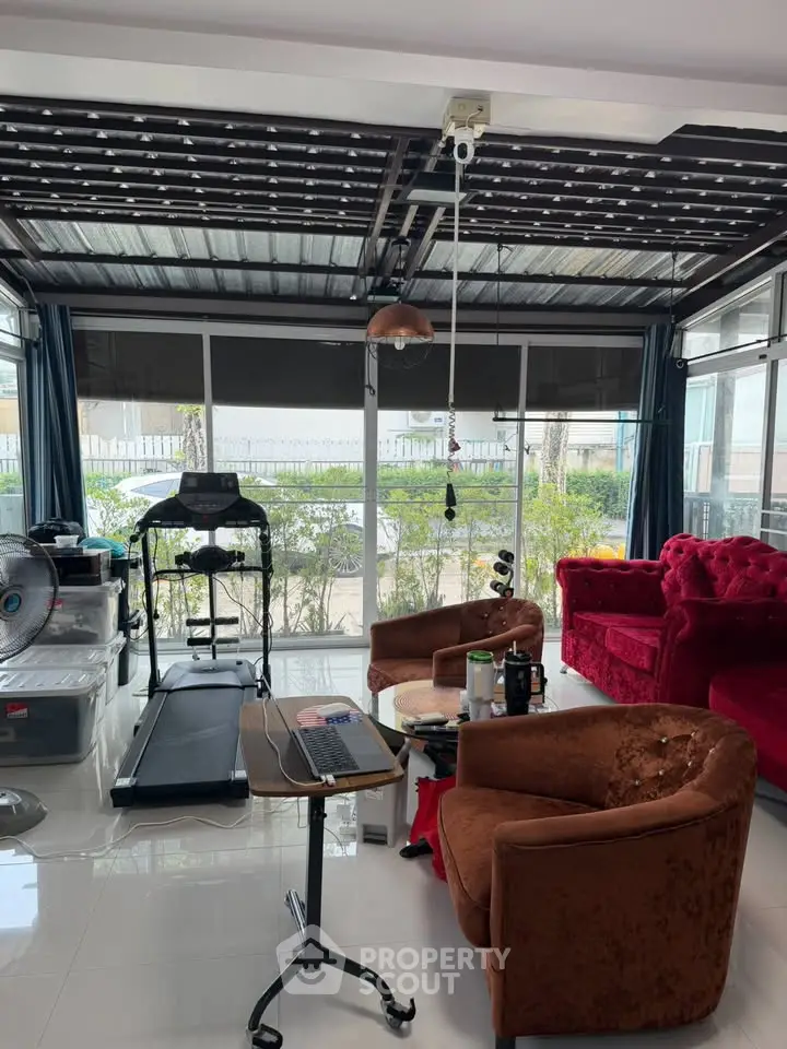 Spacious living room with treadmill and cozy seating area, featuring large windows and modern decor.