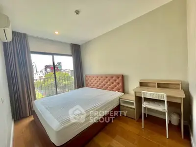 Spacious bedroom with large window and modern furnishings in a city apartment.