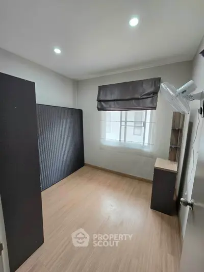Spacious bedroom with wooden flooring and ample natural light from large window.