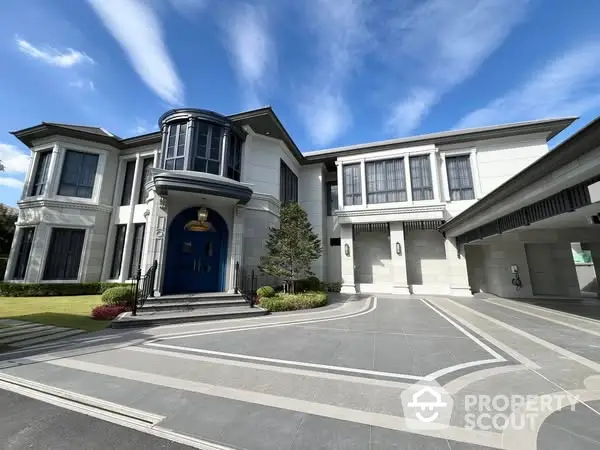 Luxurious modern mansion with grand entrance and spacious driveway under clear blue sky.