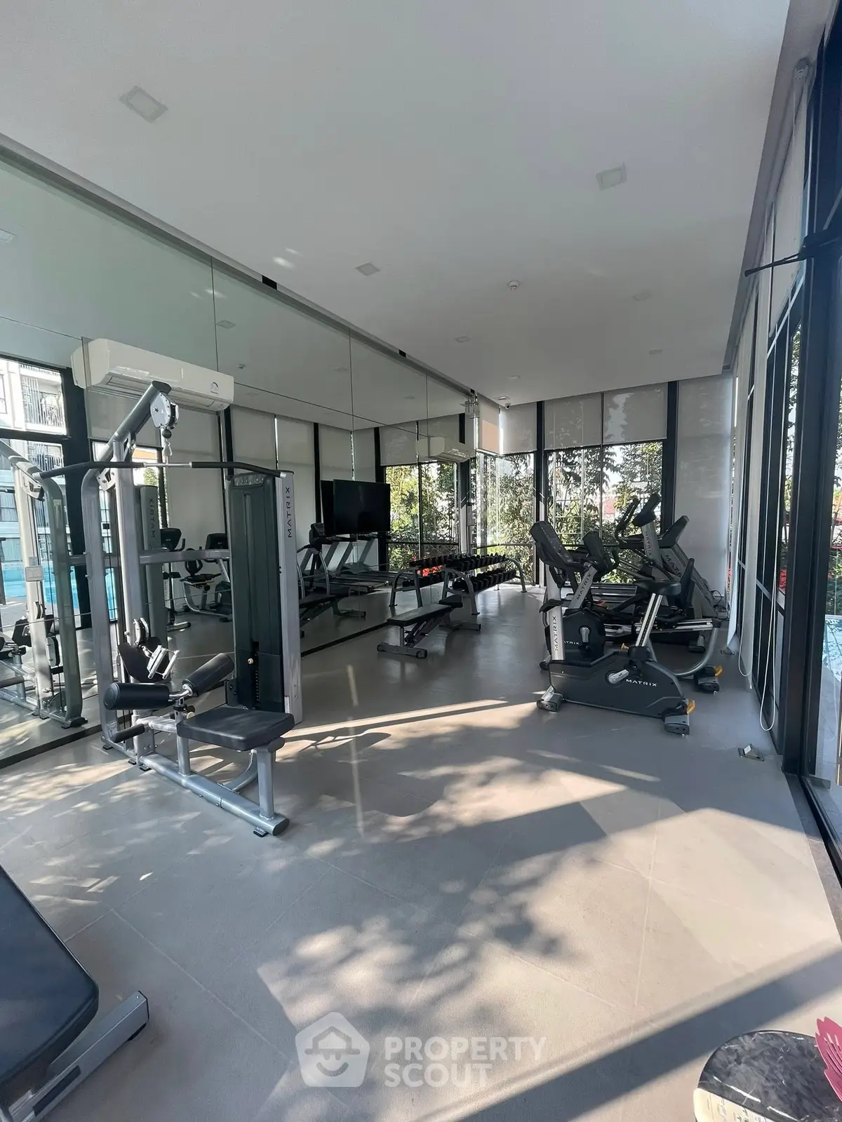 Modern gym with state-of-the-art equipment and floor-to-ceiling windows in luxury building.