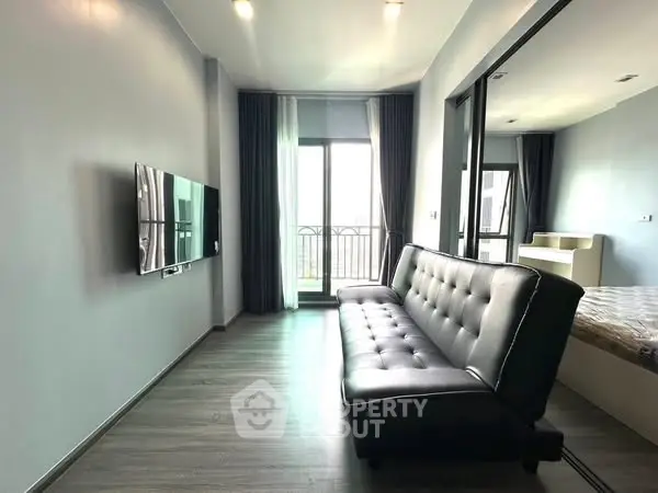 Modern living room with sleek black sofa and wall-mounted TV, featuring a balcony view.