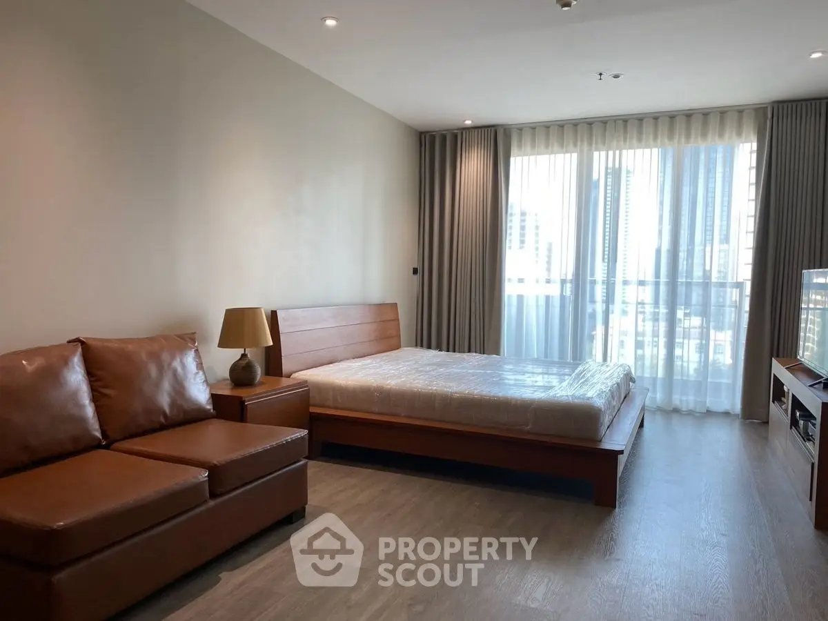 Spacious modern bedroom with large window and stylish furniture in urban apartment.