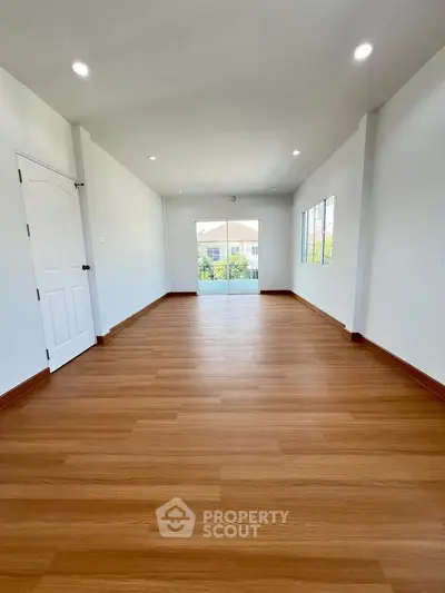 Spacious empty room with wooden flooring and large windows offering natural light.