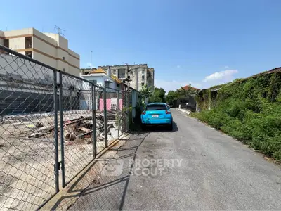 Vacant lot with potential for development in urban area, featuring adjacent road access and nearby buildings.