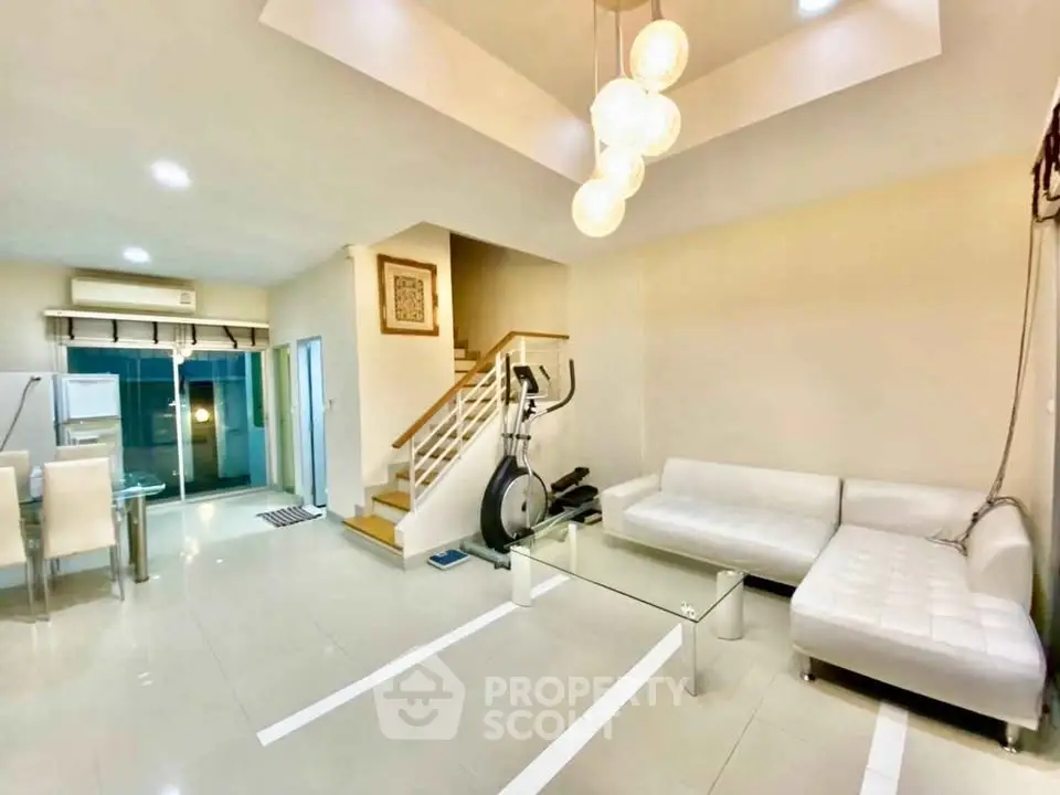 Modern living room with white sectional sofa, glass coffee table, and exercise bike in open layout.