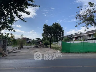 Vacant land plot with potential for development in a serene neighborhood, surrounded by greenery and clear skies.