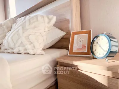 Cozy bedroom corner with wooden nightstand, decorative pillows, and a classic alarm clock.