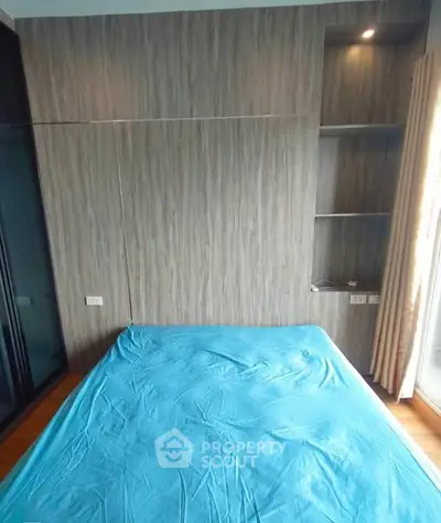 Modern bedroom with blue bedding and wooden accent wall, featuring built-in shelves and natural light.