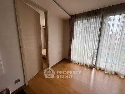 Spacious bedroom with wooden flooring and large window offering natural light and city view.