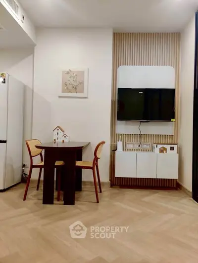 Modern dining area with stylish wooden table, chairs, and wall-mounted TV in a cozy apartment.
