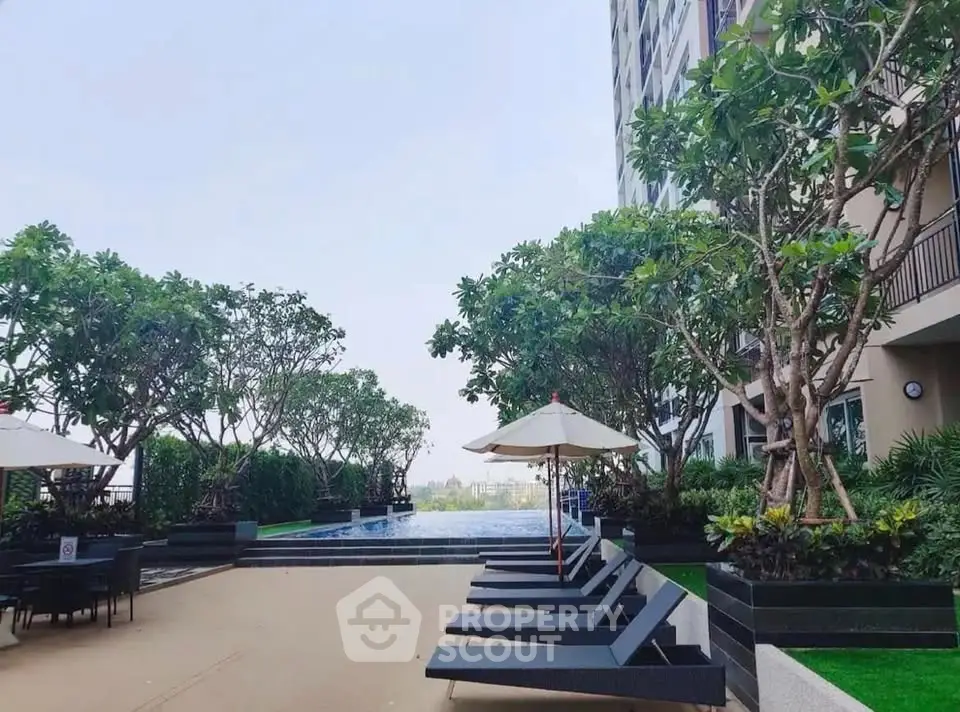 Luxurious rooftop pool area with sun loungers and lush greenery in modern apartment complex.