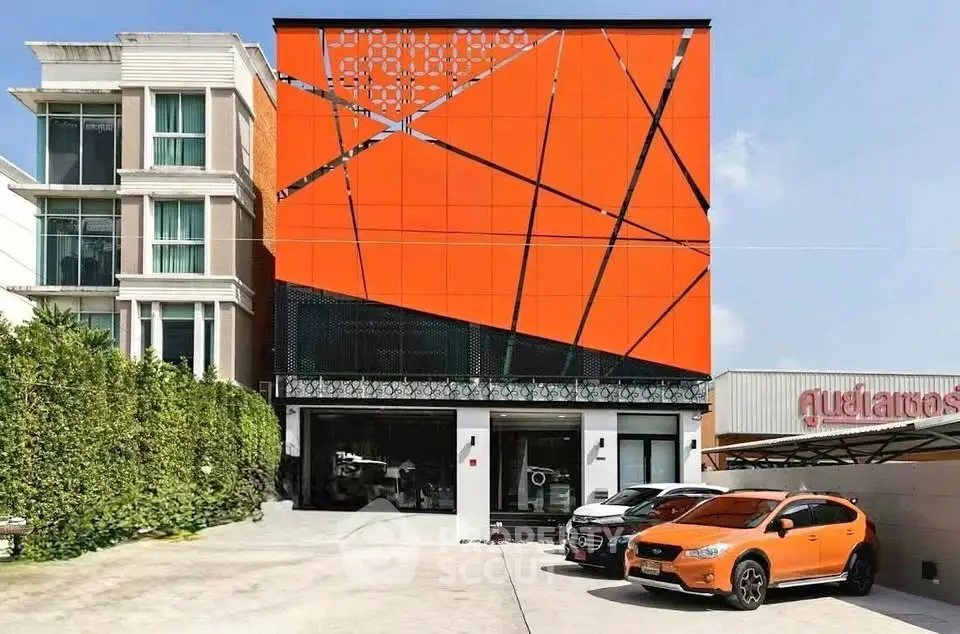 Modern building exterior with vibrant orange facade and parking area