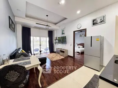 Modern open-layout living room with stylish decor and adjacent bedroom, featuring hardwood floors and natural light.