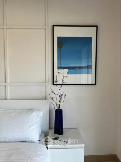 Stylish bedroom with modern decor and framed artwork, featuring a sleek white nightstand and elegant vase.