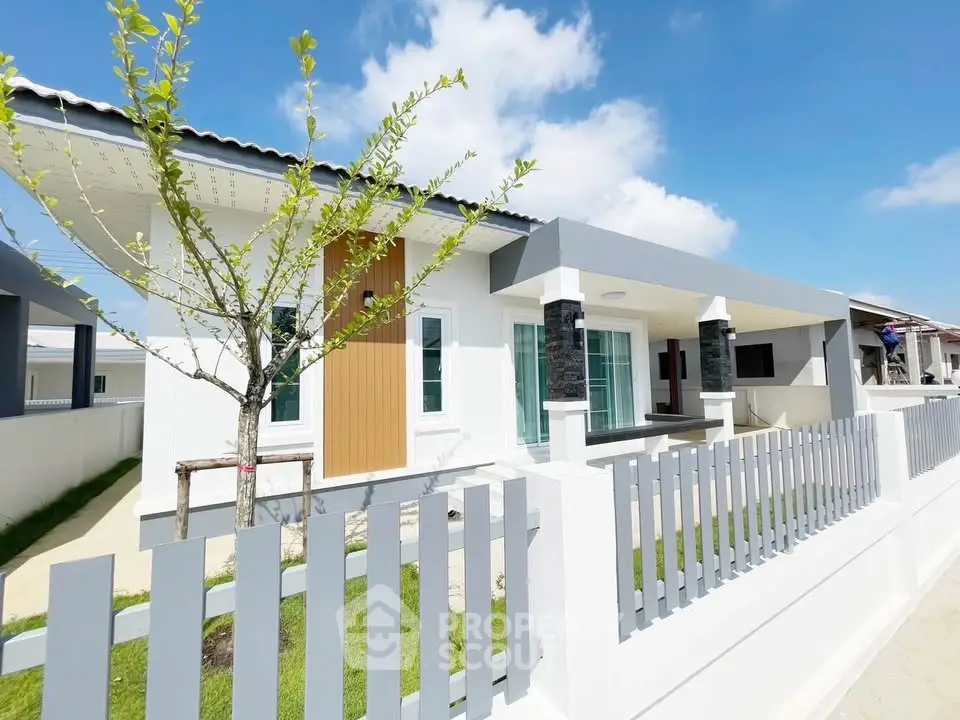 Modern single-story house with sleek design and fenced yard under clear blue sky.