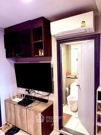 Compact living room with wall-mounted TV and view into modern bathroom.