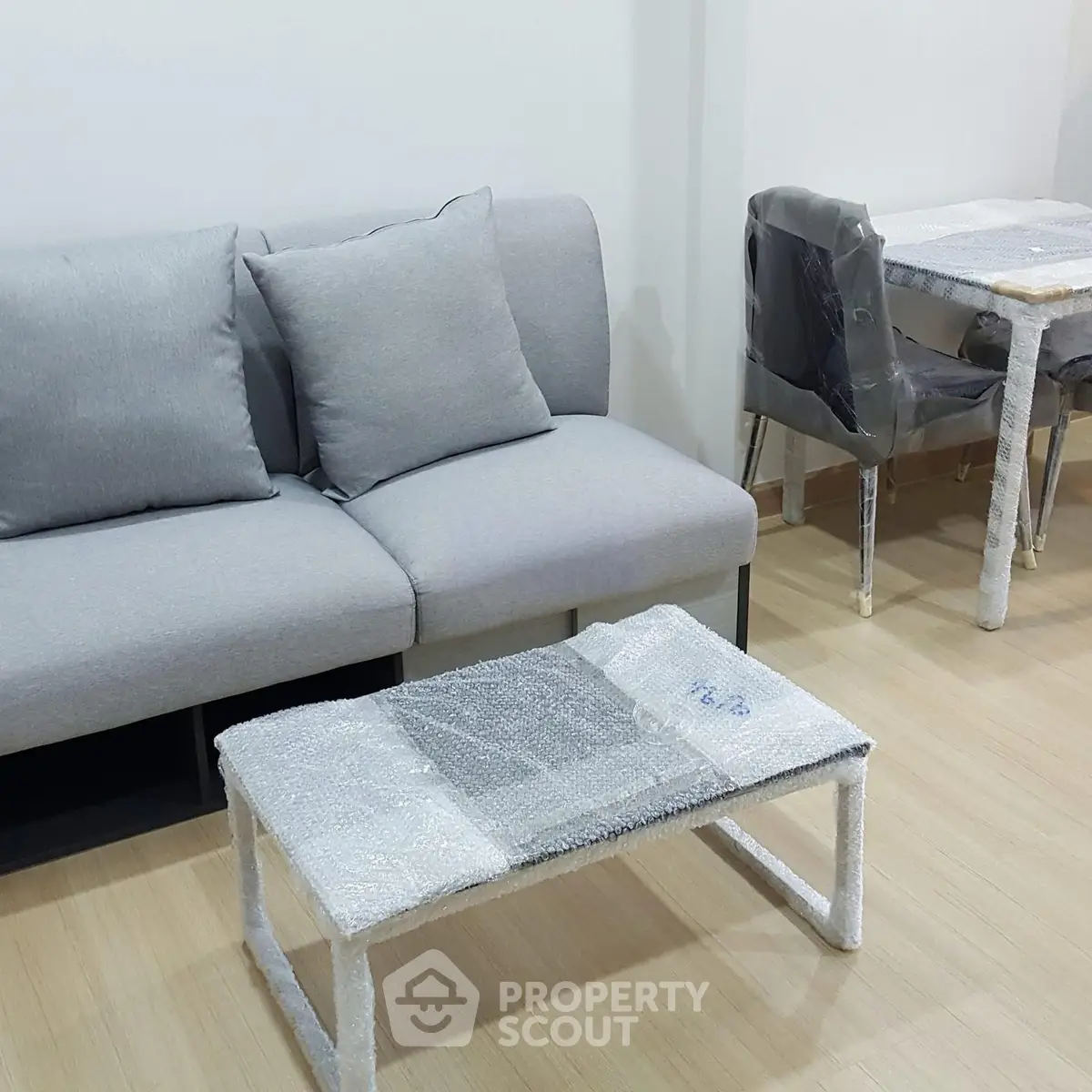 Modern living room with gray sofa and bubble-wrapped furniture, showcasing a minimalist design.