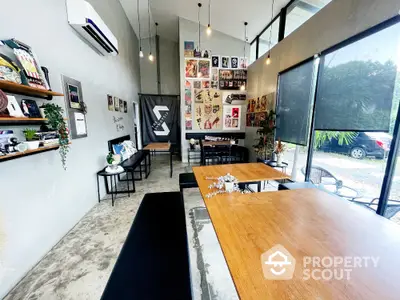 Modern industrial-style room with high ceilings and large windows, perfect for creative workspace or cafe.