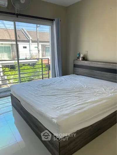 Spacious bedroom with large window and modern bed frame, offering natural light and a serene view.