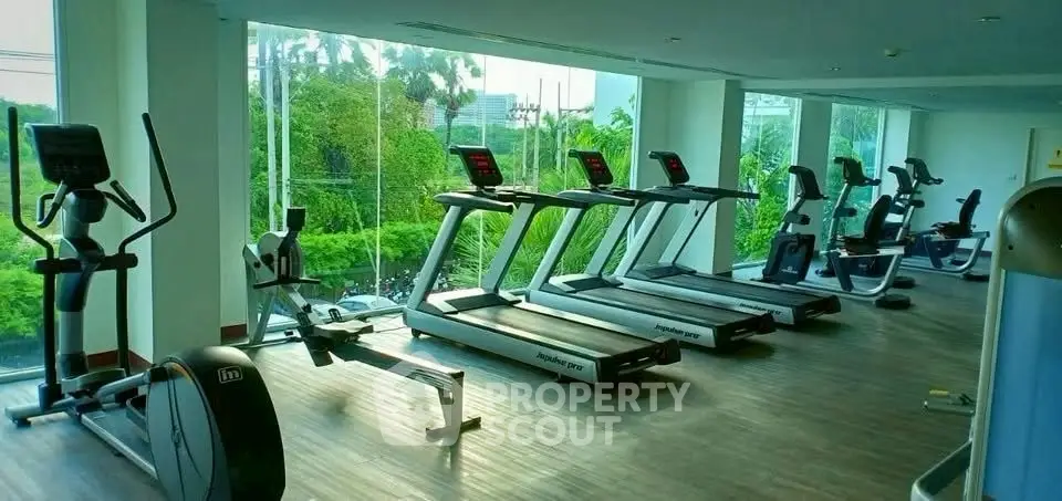 Spacious gym with modern exercise equipment and large windows offering lush green views.