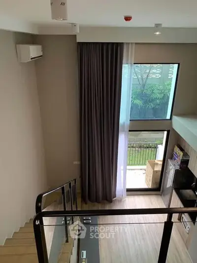 Modern loft-style living room with high ceiling and large windows overlooking a garden.