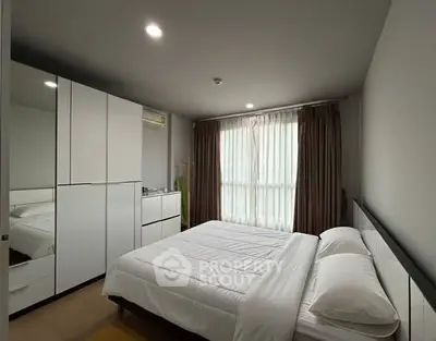 Modern bedroom with sleek white furniture and large window for natural light.