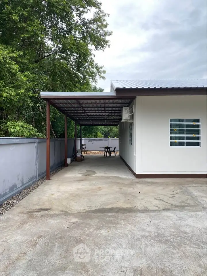 Charming single-story home with covered patio and spacious driveway, surrounded by lush greenery.