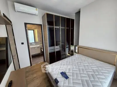Modern bedroom with glass wardrobe and air conditioning, featuring a glimpse into a stylish bathroom.