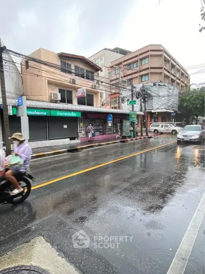 Street view of commercial buildings on a rainy day, showcasing urban real estate potential.