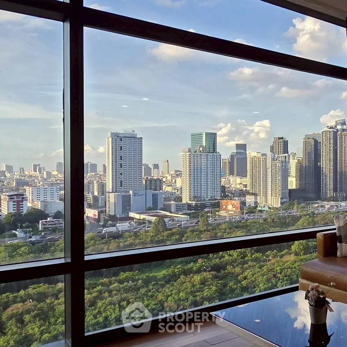 Stunning cityscape view from a modern high-rise apartment window, showcasing urban skyline and lush greenery.